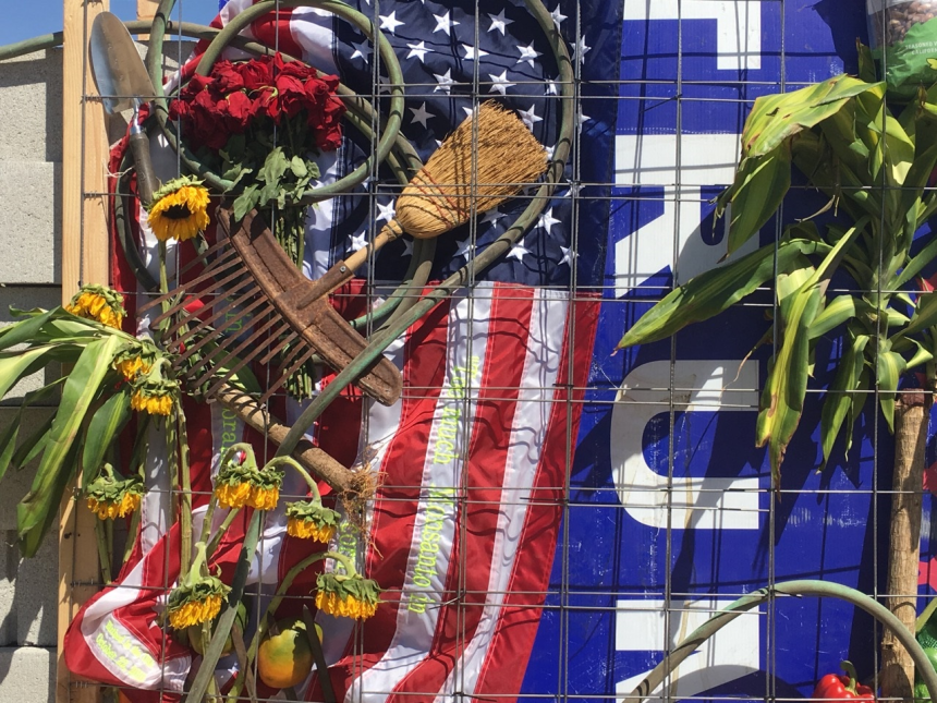 Elementos agrícolas, una bandera y un cartel de Trump en muro anti-Trump